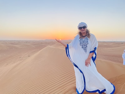 A flowing North African kaftan displayed against a backdrop of desert dunes at sunset.