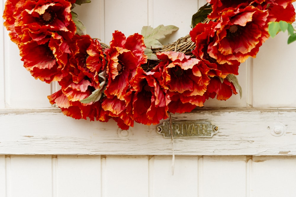a wreath with red flowers on a white door