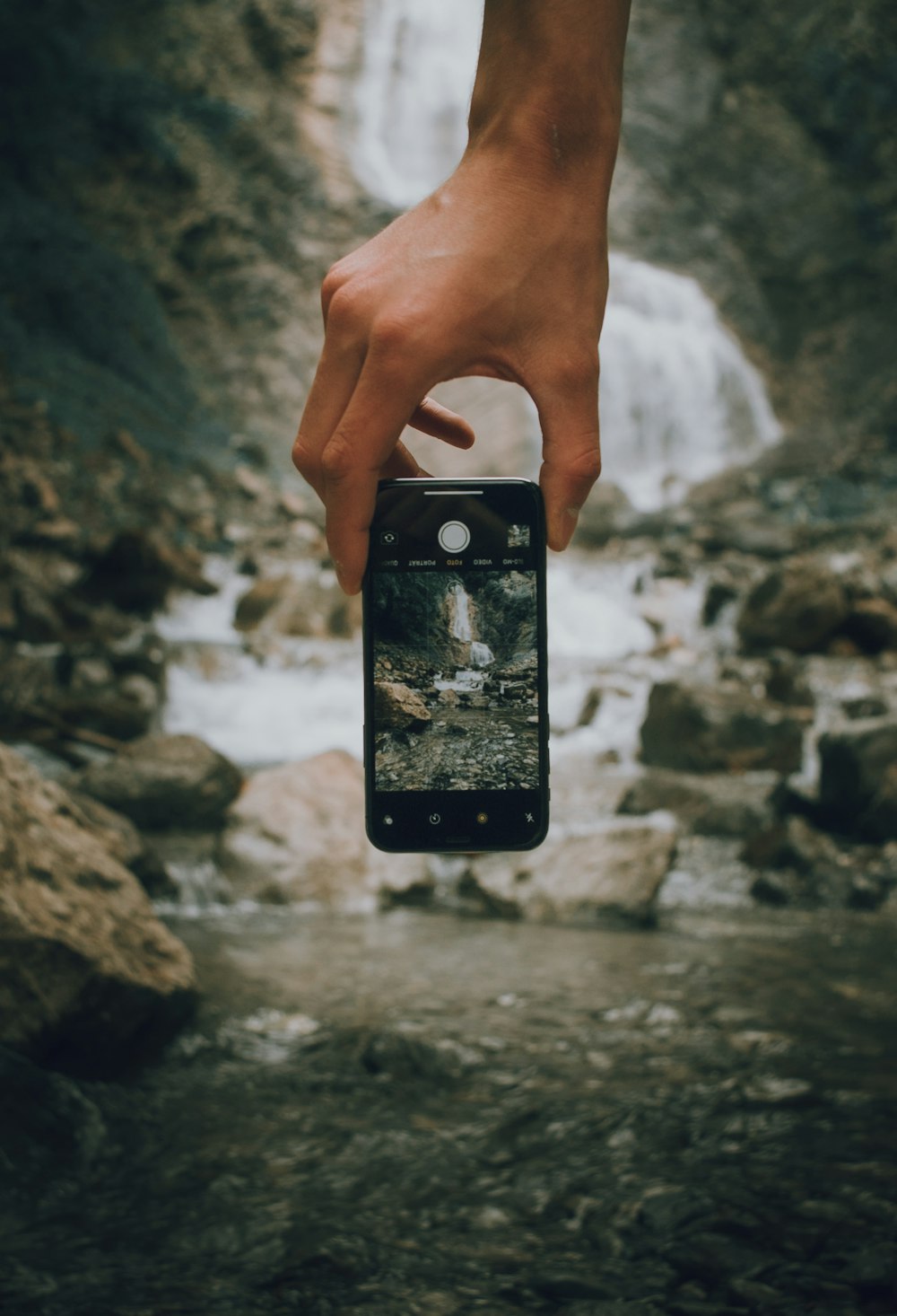 a person holding a cell phone in front of a waterfall