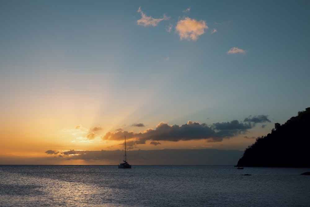 the sun is setting over the ocean with a boat in the water