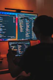 a man sitting in front of two computer monitors