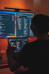 a man sitting in front of two computer monitors