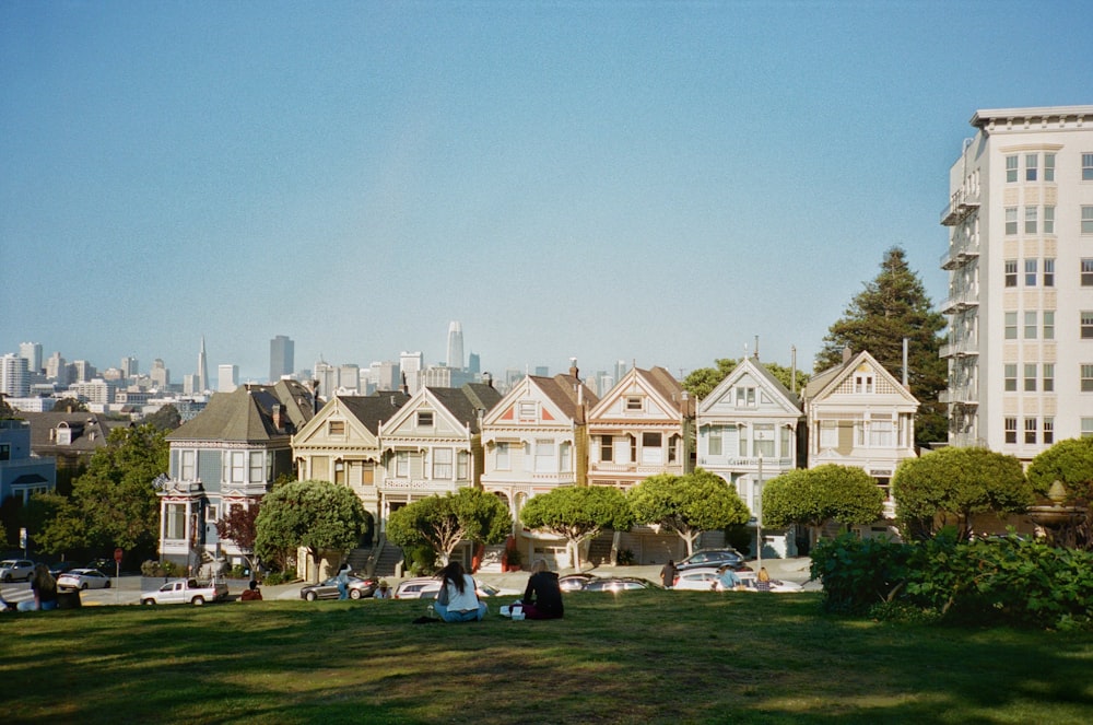 a group of people sitting on the grass in front of a row of houses