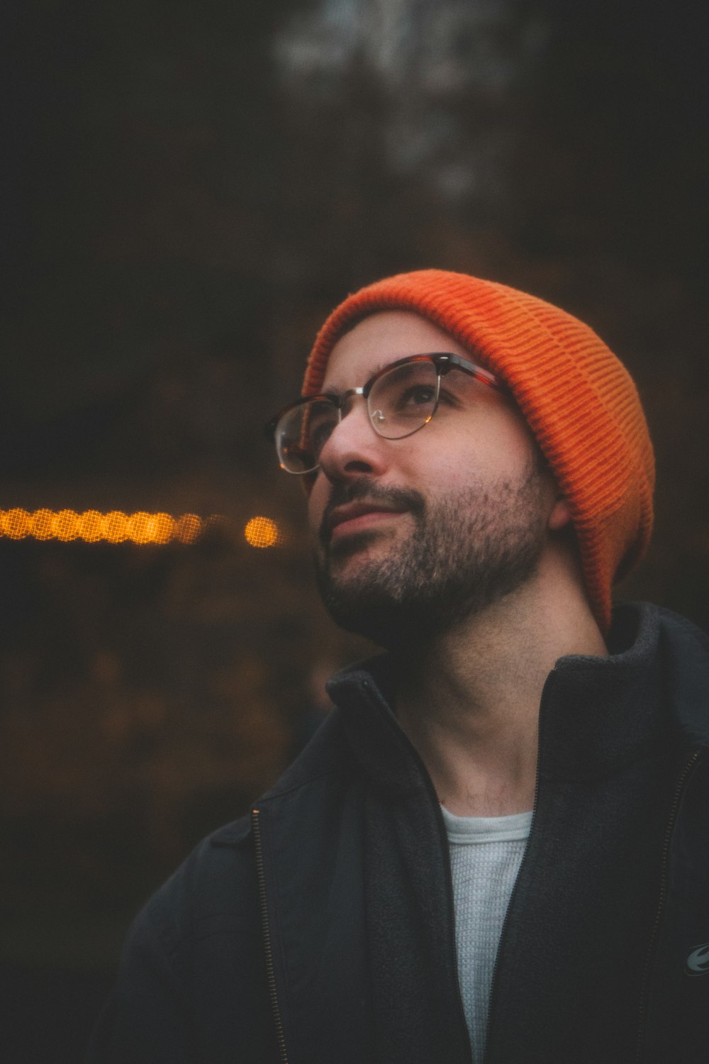 a man wearing a beanie and glasses looks off into the distance