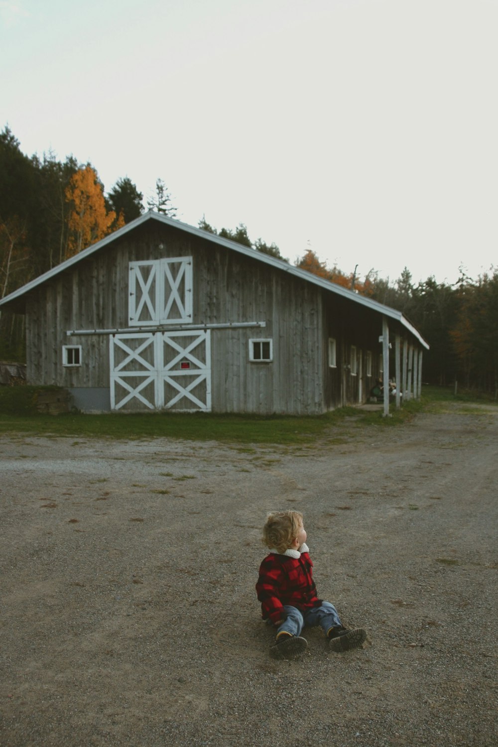 a little boy sitting on the ground in front of a barn