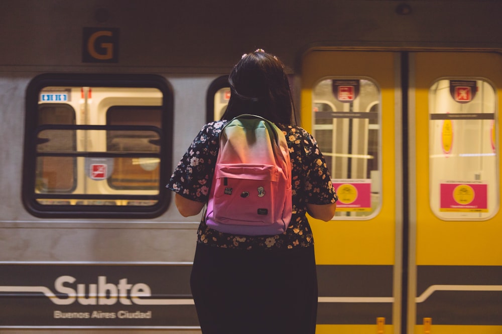 uma mulher com uma mochila cor-de-rosa em pé na frente de um trem