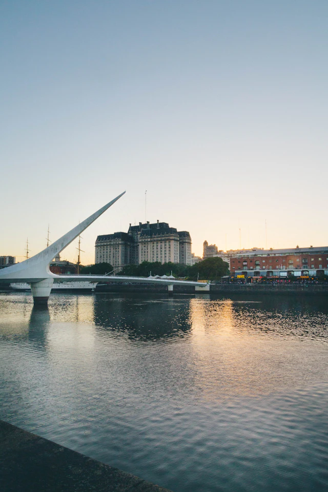 The white sail-shaped Puente de la Mujer footbridge reflected in the still water of the Puerto Madero dock at dawn.