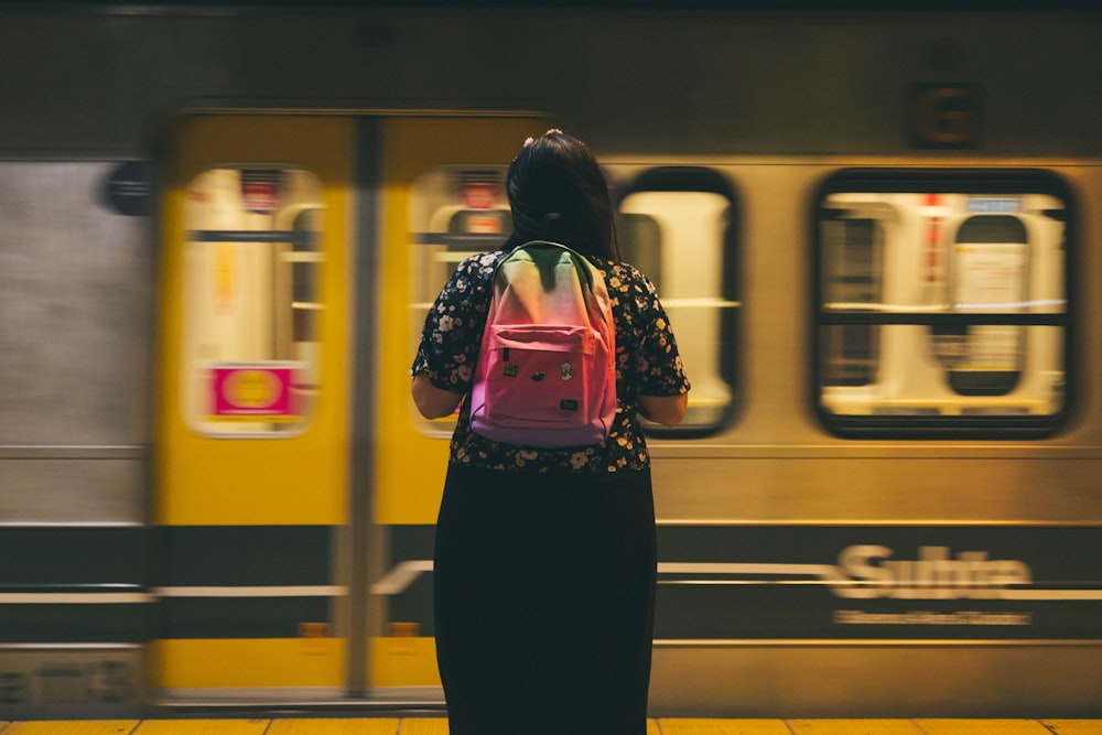 a woman with a pink backpack waiting for a train