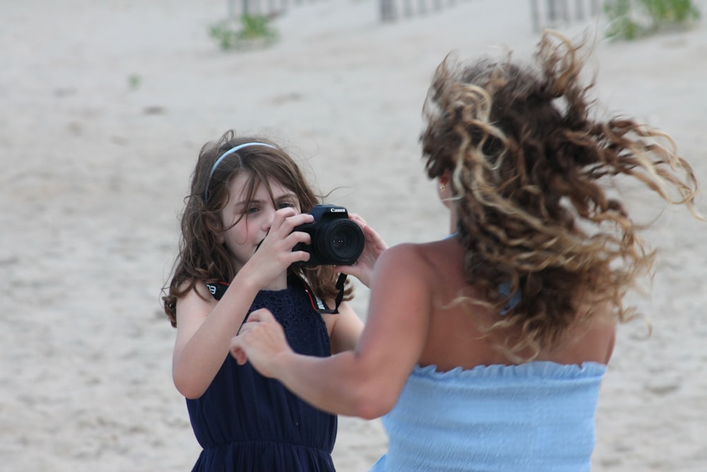 a woman taking a picture of a little girl on the beach