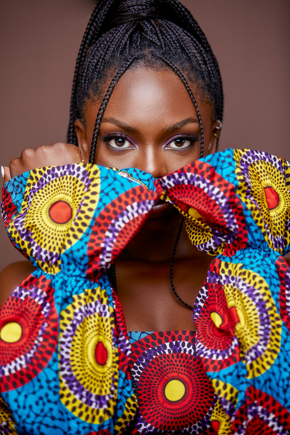 a woman with braids holding a colorful cloth over her face