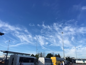 A fleet of buses parked at a bus terminal under a clear blue sky.