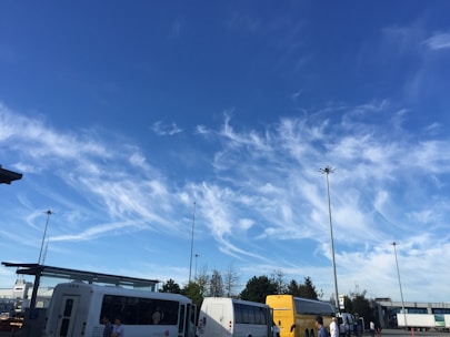 A fleet of buses parked at a bus terminal under a clear blue sky.