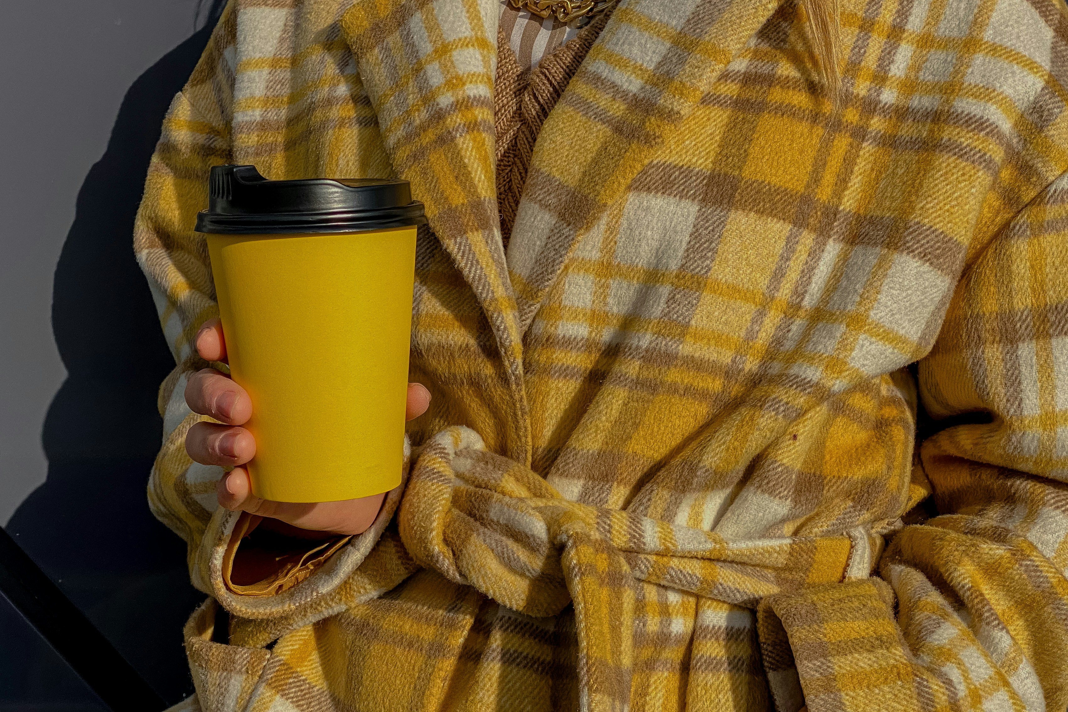 Woman in an autumn plaid coat holding a yellow cup with takeaway coffee. Cup mockup 
