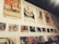 A wall display featuring vintage movie posters and album covers. The posters are arranged in two horizontal rows, with the top row consisting of large movie posters showcasing various films, some with retro themes. Below them are smaller images, likely related to films or music, and a series of vinyl records or album covers displayed on a shelf. The overall aesthetic is nostalgic, reminiscent of mid-20th century pop culture.