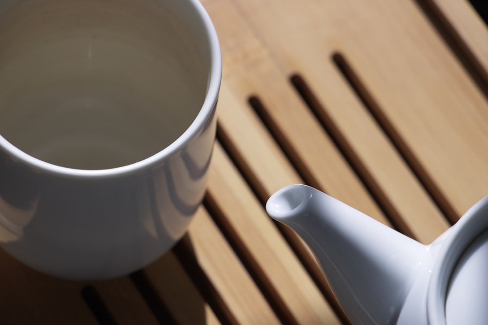 a white teapot and a white cup on a wooden table