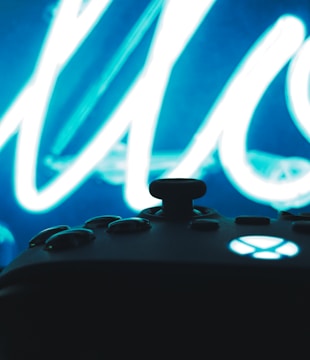 A silhouetted view of a gaming controller with a glowing button is set against a bright, abstract blue and white neon background.