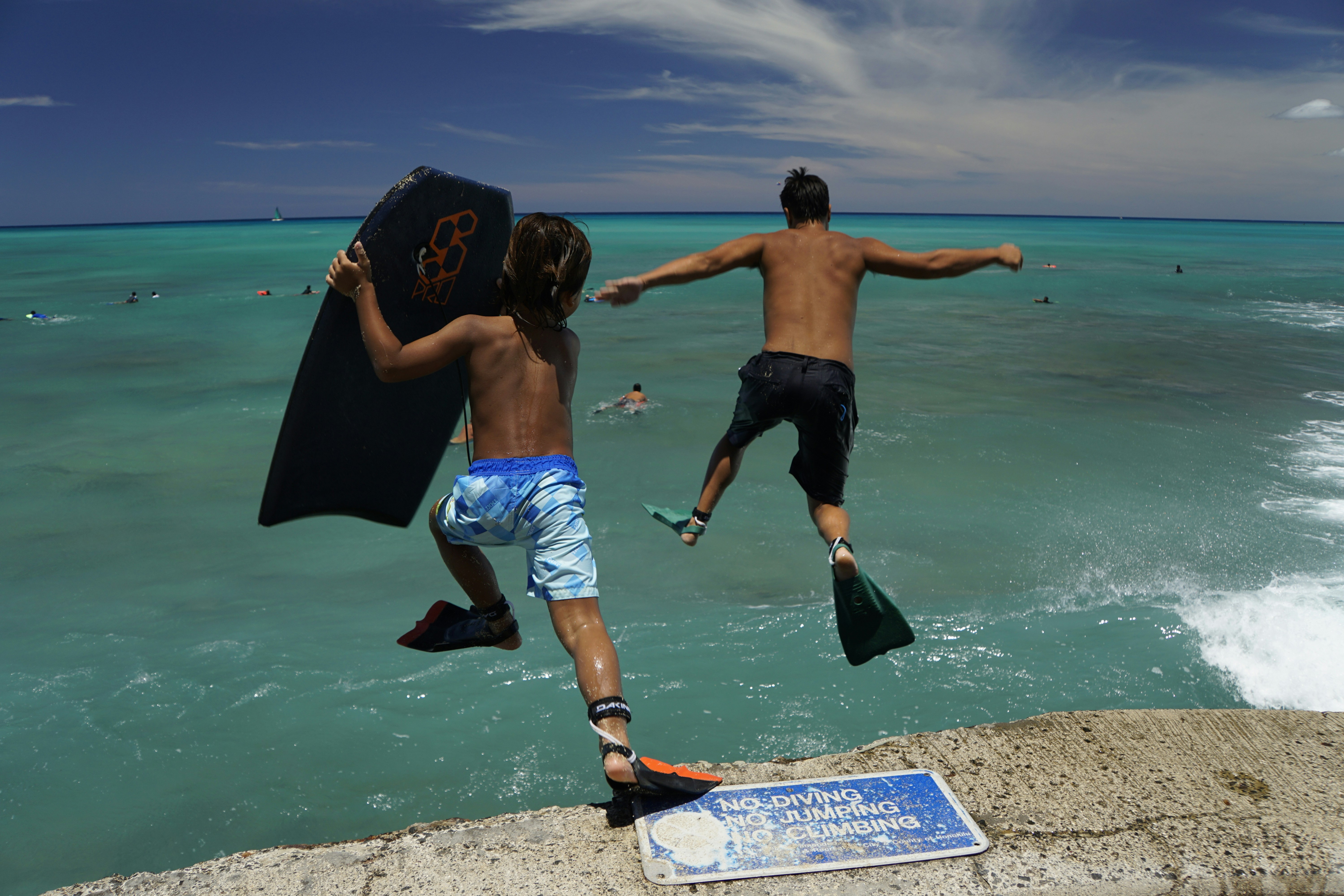 two people jumping into the ocean from a cliff
