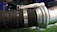 A close-up view of a heavy-duty metal pipe connection featuring a large rubber hose secured with metal clamps. The components display industrial material textures with a combination of metallic and rubber surfaces.