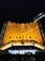 A grand hotel building illuminated with warm orange lights at night. The main facade features tall windows arranged in a geometric pattern and numerous flags flying in the front. The sign 'Plaza Indonesia' is prominently displayed in glowing letters above an entrance area surrounded by dark foliage.
