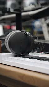 A pair of high-end studio reference headphones resting on a wooden desk beside a vintage keyboard.