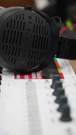 Stylish black and gold headphones resting on a mixing console in a dimly lit studio.