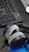A pair of plush, over-ear headphones resting on a desk near a computer keyboard. The keyboard is black and has a wired connection. A blue notepad or document is partially visible beneath the headphones.