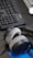A pair of plush, over-ear headphones resting on a desk near a computer keyboard. The keyboard is black and has a wired connection. A blue notepad or document is partially visible beneath the headphones.