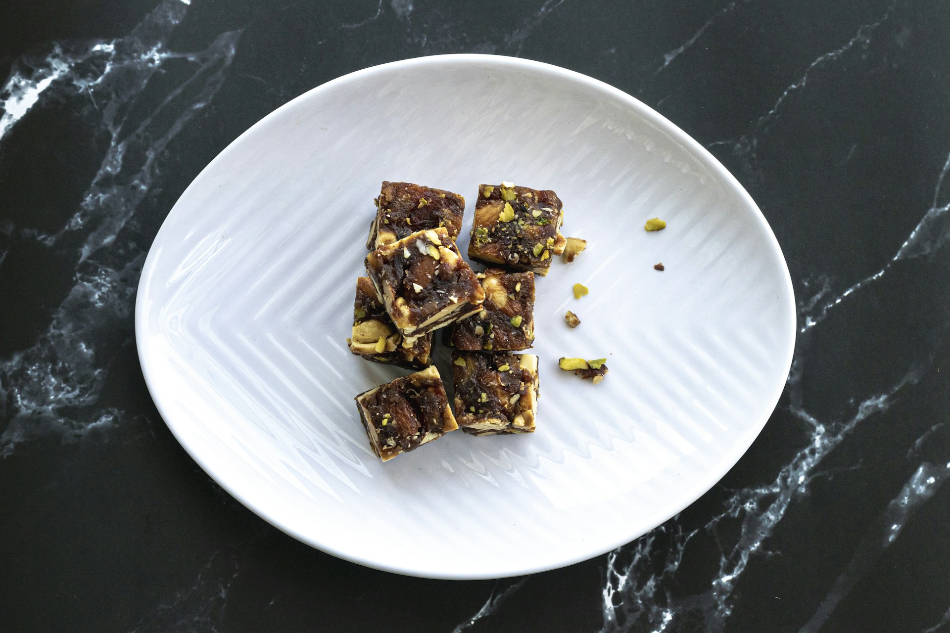 An elegant display of keto peanut brittle pieces, glistening with caramel and sprinkled with crushed nuts, arranged on a dark slate board.