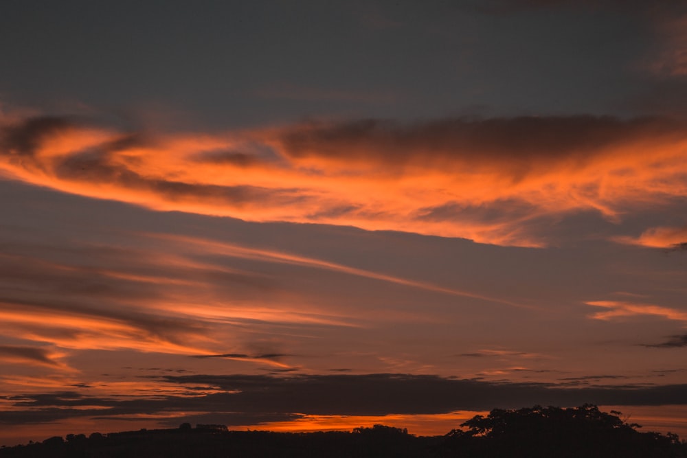 a sunset with clouds in the sky and trees in the foreground