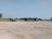 Several small aircraft are parked on a large open tarmac under a clear blue sky. There are a few trees and grass visible in the background. A person can be seen near the planes, possibly performing maintenance or inspection.