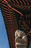 A detailed architectural roof design rich in colors and patterns with a focus on traditional elements. Below the roof, a stone statue resembling a lion is positioned prominently, displaying intricate carvings and a texture typical of historic sculptures.