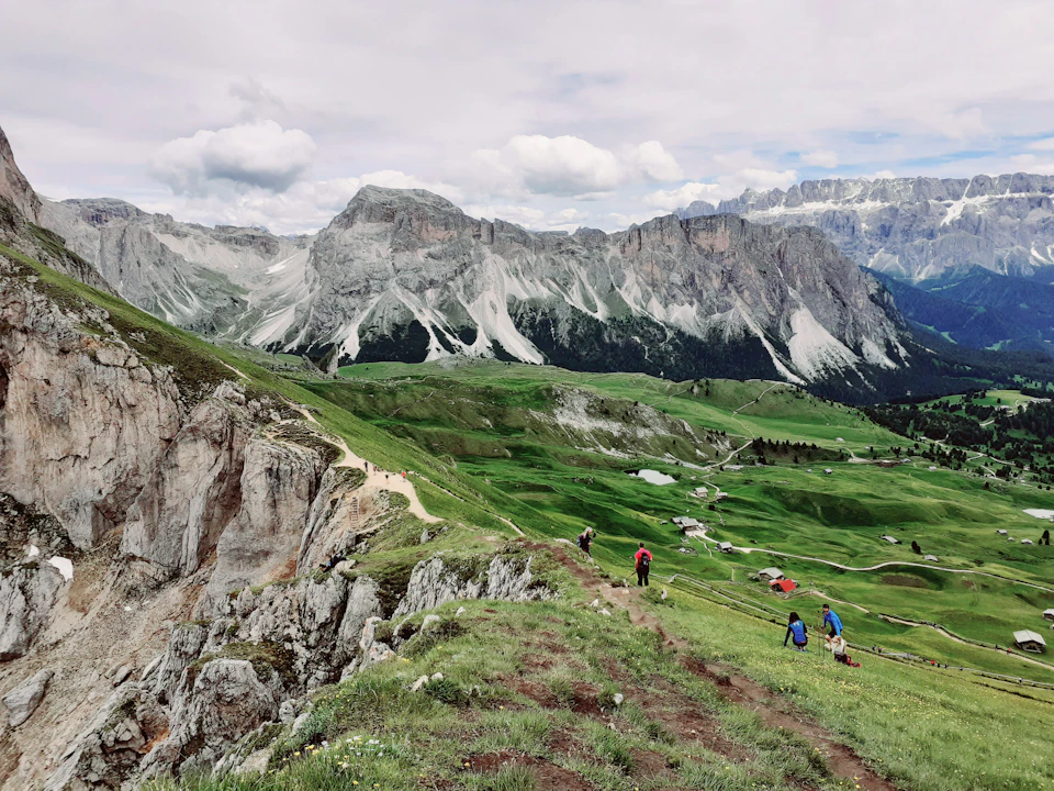 Group of hikers ascending steep rocky mountain trail with backpacks and walking sticks nearby