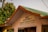 The image depicts a building with a sign in both Hindi and English that says 'Reception & Buddhist Information Counter'. It is part of the Mulagandha Kuty Vihara, Sarnath, Varanasi (UP). The roof is green with orange trim, and there are lush green trees in the background, along with a palm tree. The atmosphere appears sunny and peaceful.