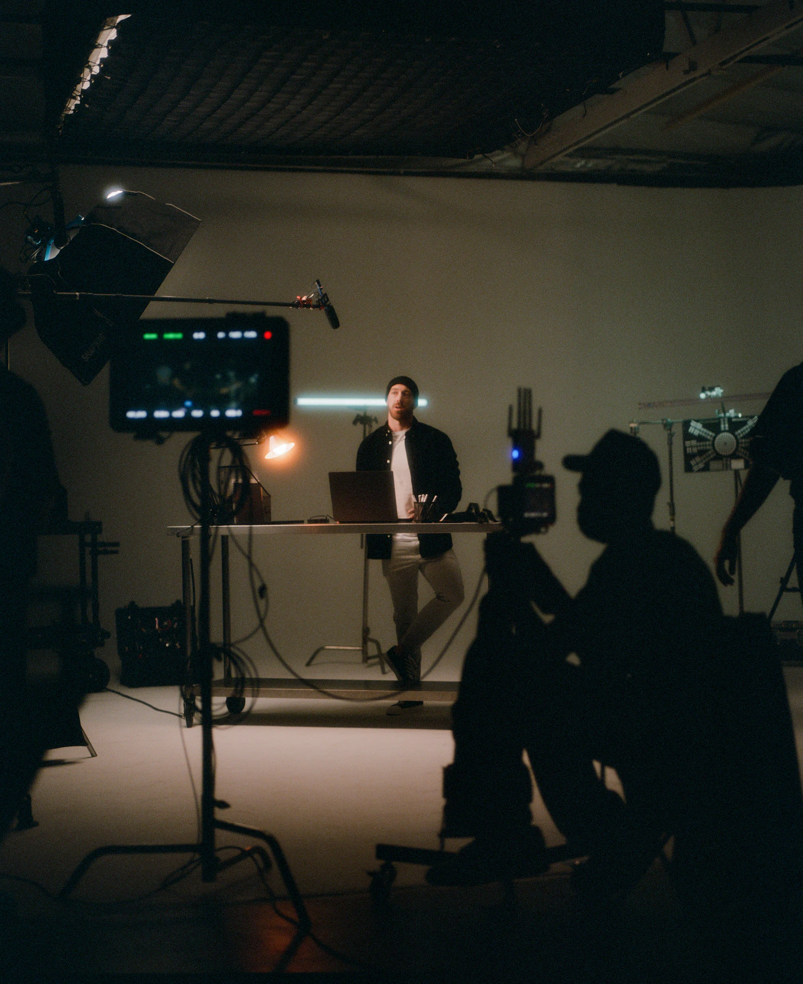 A man working at a laptop while a camera operator films him, a monitor and boom microphone in frame