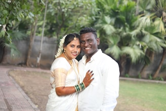 Lifestyle shot of a couple dressed in matching bridal gharara and suit, smiling in a garden setting.