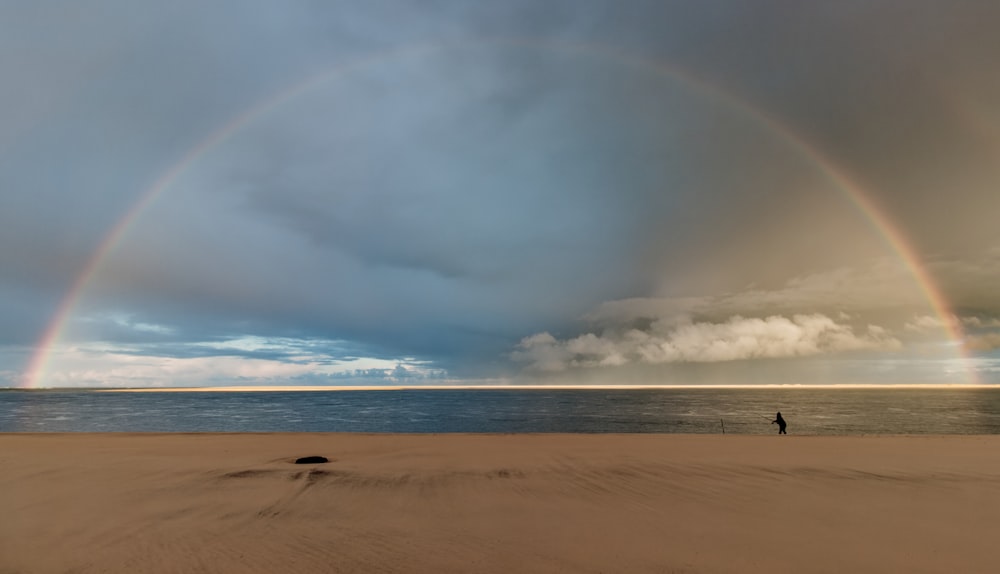 a person standing on a beach under a rainbow