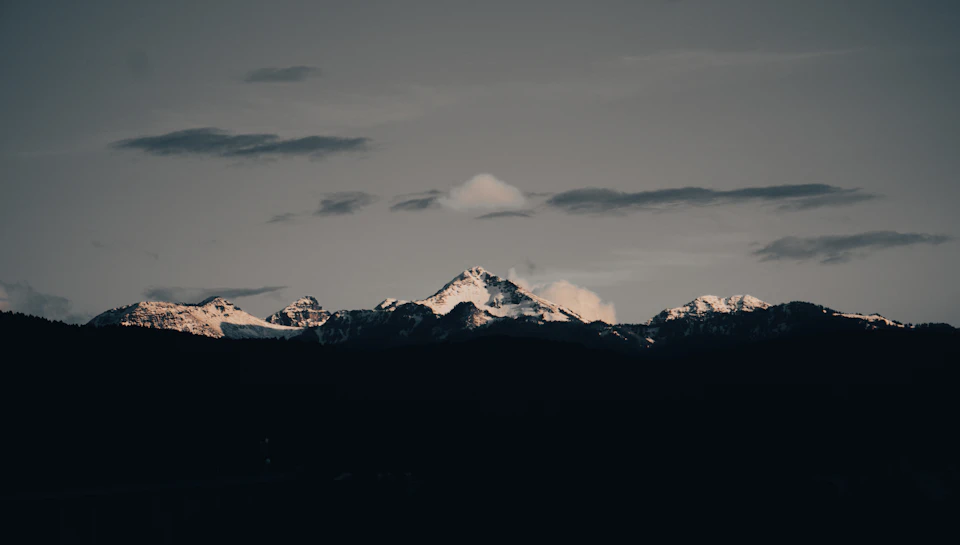 Mountain range under cloudy sky with three snow-capped peaks standing tall in gray expanse