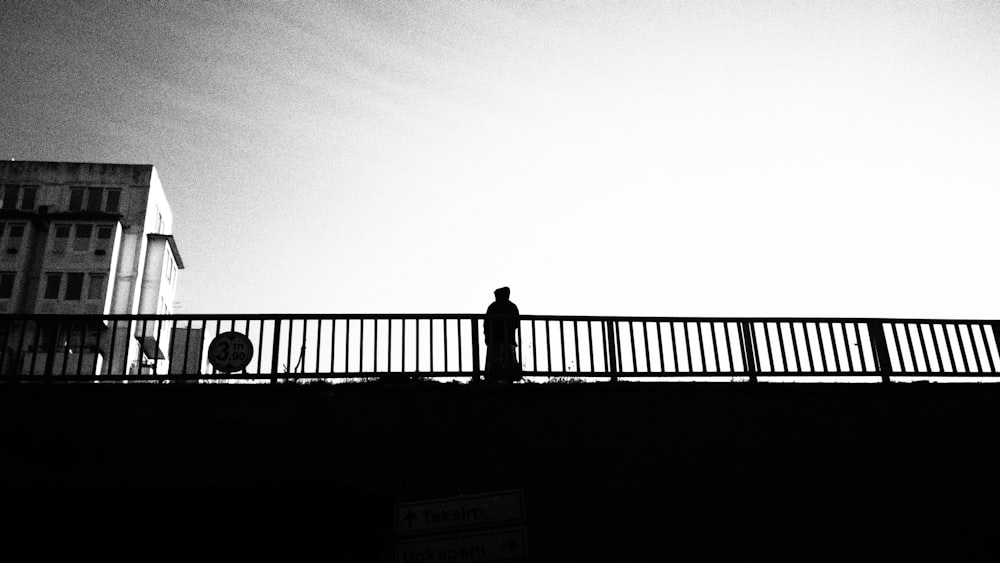 Una foto in bianco e nero di una persona in piedi su un ponte
