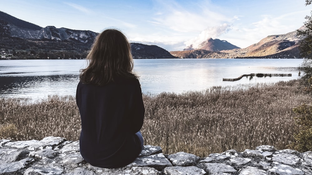 Eine Frau sitzt auf einem Felsen und blickt auf einen See