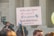 A protest sign held by someone in front of a large stone building with columns, advocating a pro-life message related to abortion. The sign reads, 'Hello, yes, I have a uterus, an opinion. End abortion.' A crowd is gathered, and some individuals are visible wearing security or official uniforms.