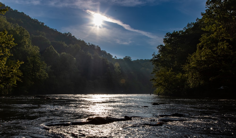 the sun shines brightly over a river surrounded by trees