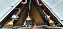 A close-up view of industrial equipment featuring a complex structure of metallic pipes and coils. Copper tubes are prominently visible, along with mechanical components and wiring neatly organized within a triangular frame.