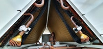 A close-up view of industrial equipment featuring a complex structure of metallic pipes and coils. Copper tubes are prominently visible, along with mechanical components and wiring neatly organized within a triangular frame.