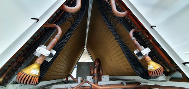 A close-up view of industrial equipment featuring a complex structure of metallic pipes and coils. Copper tubes are prominently visible, along with mechanical components and wiring neatly organized within a triangular frame.