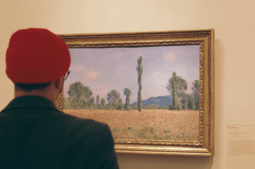 a man in a red hat looking at a painting