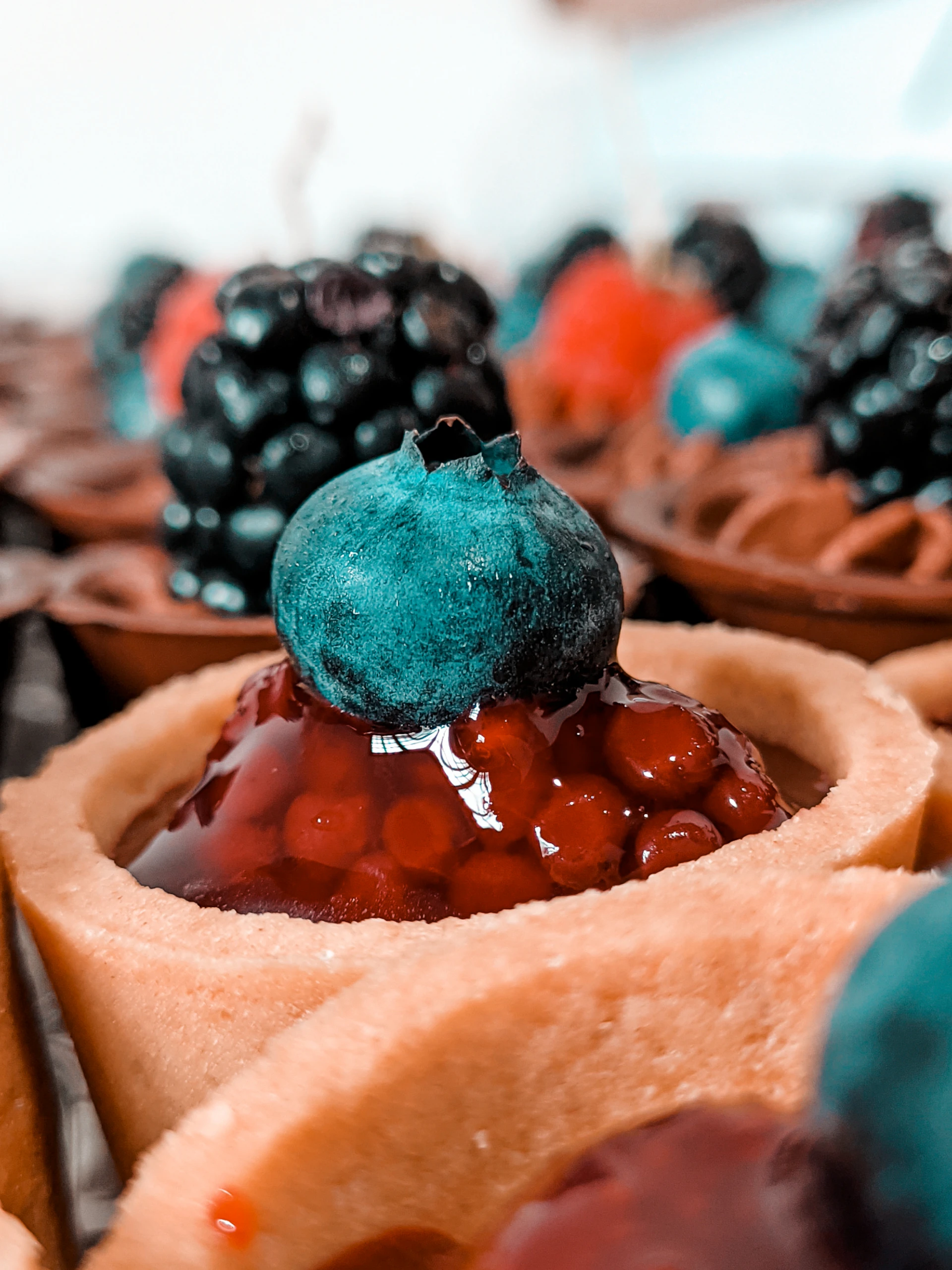 Close-up of a delicate, minimalist berry tart with glossy fresh strawberries and blueberries on a simple white plate.