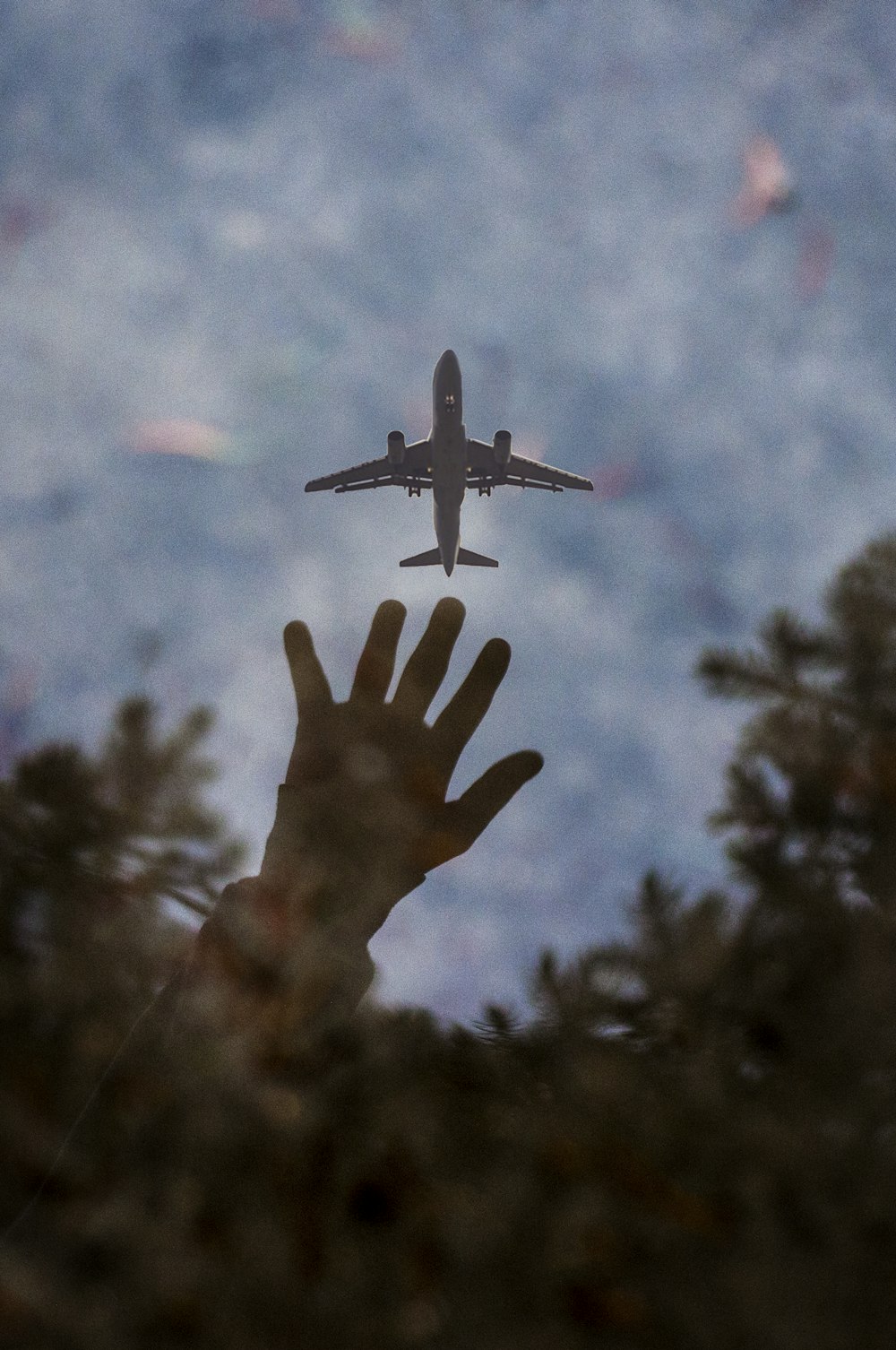 a person's hand reaching up to a plane in the sky