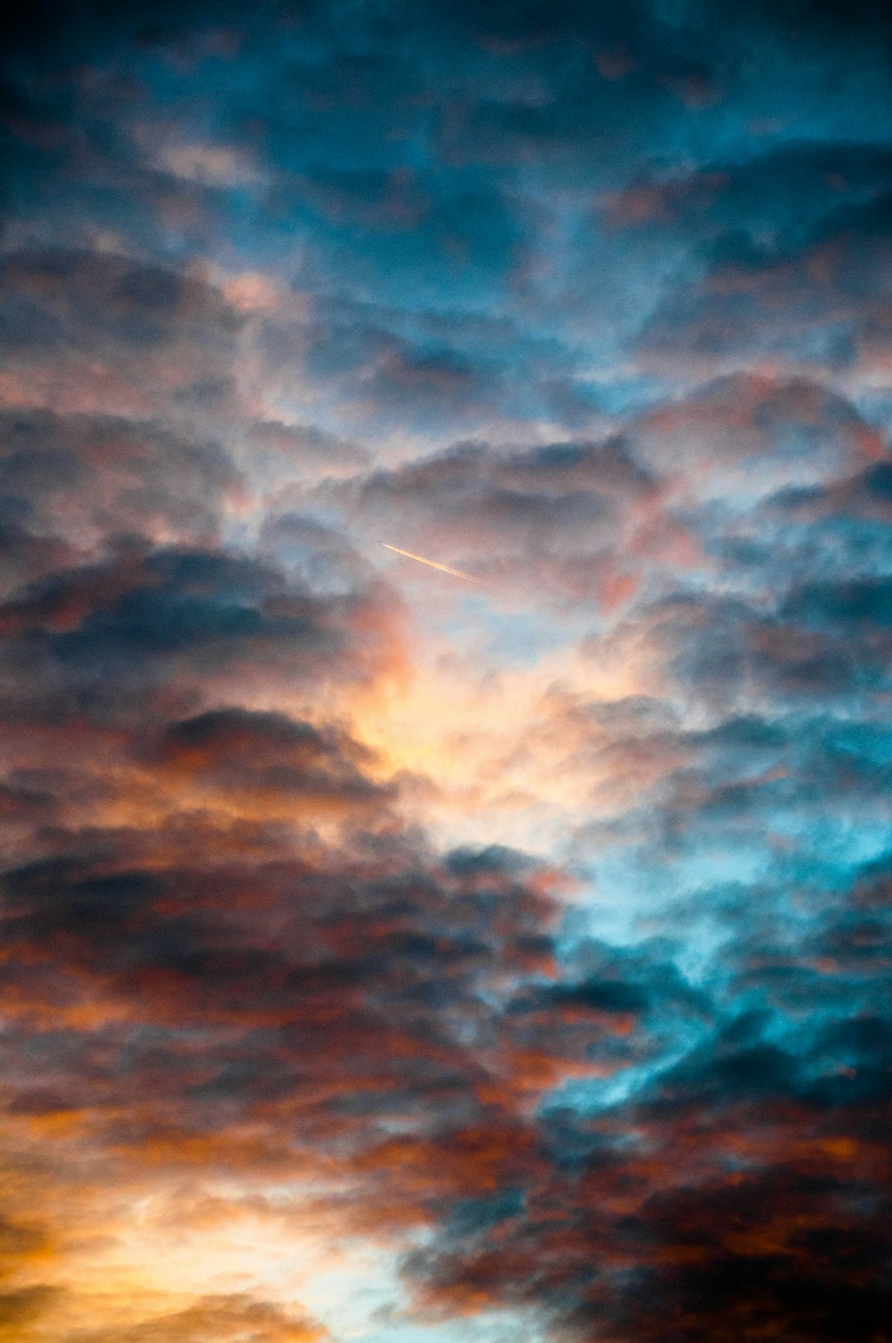 a plane flying through a cloudy sky at sunset