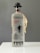 A bottle of Fiddler Vodka is displayed, featuring a frosted glass design with silhouette of a fiddler and dancers. It has a black cap shaped like a bowler hat and a tag attached to the neck. The label includes details of its production in Krakow and the alcohol volume.