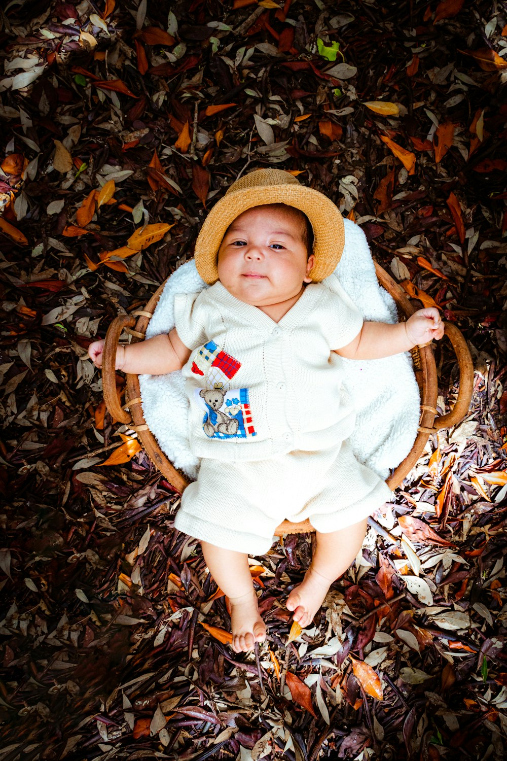 a baby wearing a white outfit and a hat sitting in a basket
